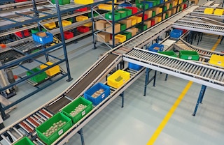 Een circuit van transportbanen voor dozen verbindt de stellingen met de pickstations